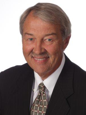 Donald Tuttle older man with grey hair wearing a black suit white shirt and brown pattern tie